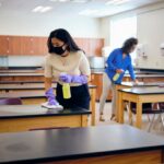 Cleaning staff sanitizing classroom desks with disinfectant spray for a hygienic learning environment.